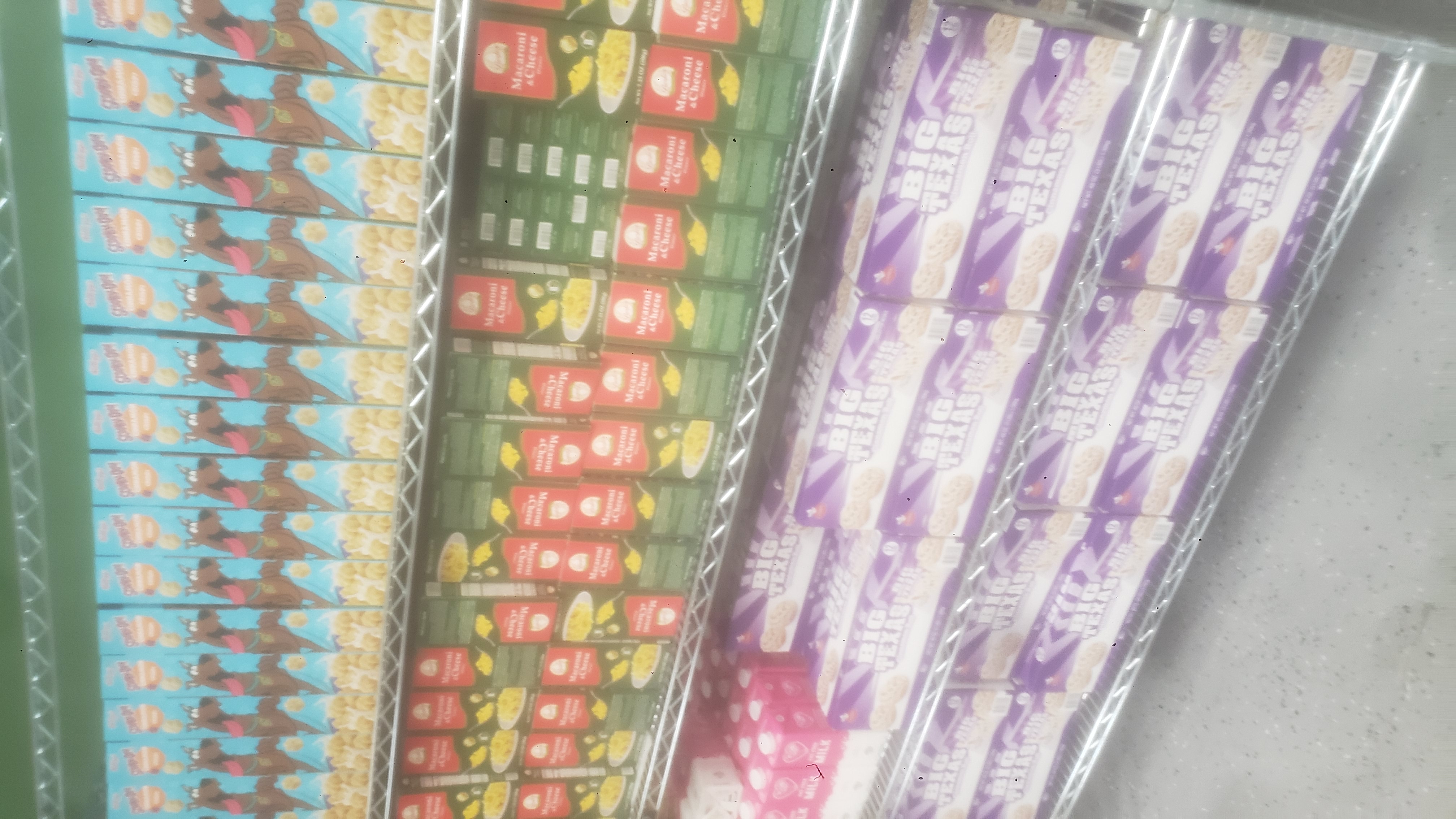 Boxes of mac n cheese, boxes of cinnamon rolls, cartons of fat-free milk on a shelf, and boxes of cinnamon crisp cereal in a shelf.